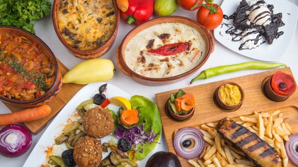 Više tradicionalnih jela Restorana Gradska Beograd, zemljane posude, predjela, glavno jelo, pomfrit i desert na jednom stolu.